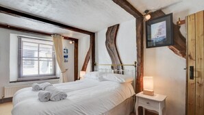 Een slaapkamer met een groot bed, een nachtkastje met een lamp, een raam met gordijnen en een houten balk aan het plafond.