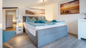 Un dormitorio con una cama, una mesita de noche, una lámpara, una silla y obras de arte en las paredes.