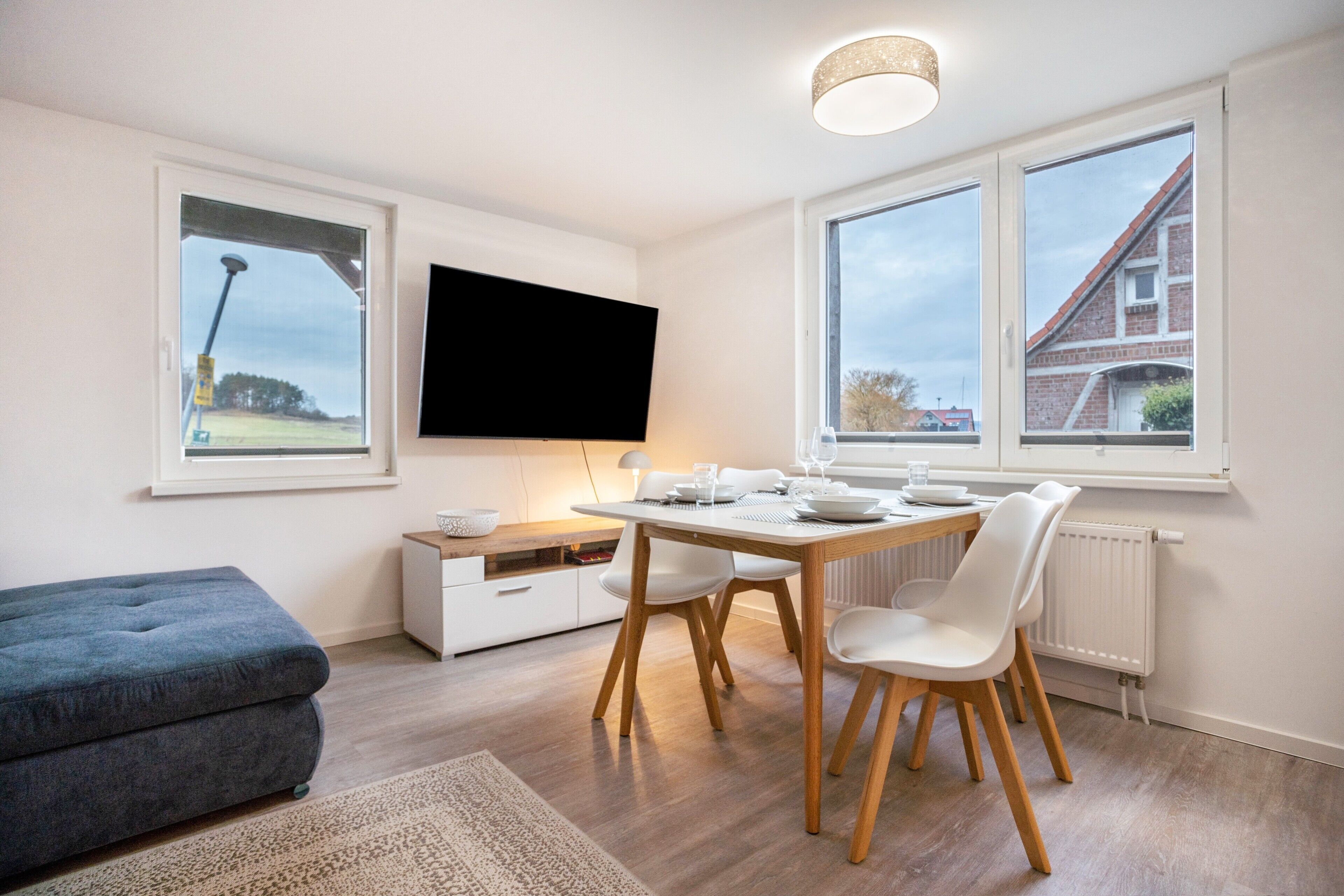 Una sala de estar moderna con comedor, un televisor de pantalla plana montado en la pared y grandes ventanales con vistas al exterior.