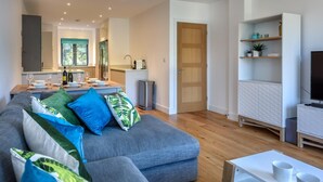 Un espace de vie moderne avec un canapé gris, un coin repas avec une table dressée pour quatre personnes et un téléviseur posé sur un meuble.