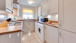 Une cuisine moderne avec des meubles blancs, un four à micro-ondes, une bouilloire et un lave-linge.
