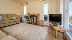 A living room with a sofa, a fireplace, a TV, and a large window. - 2 Bed in Bwlchtocyn (oc-brynxx) (Bwlchtocyn)