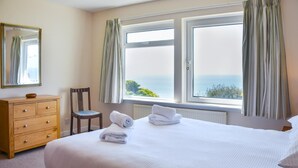 Quarto com cama, cómoda de madeira, cadeira e janela com cortinas.