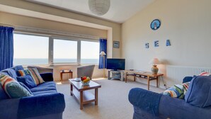 Sala de estar com sofá, televisão, luminária e vista para o mar.