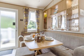 A dining area with a wooden table, cushioned seating, and a view of greenery outside. - 3 Bed in Abersoch (oc-b12tal) (Abersoch)