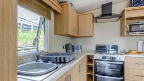 Een kleine keuken met een spoelbak, broodrooster, fornuis en houten keukenkastjes.