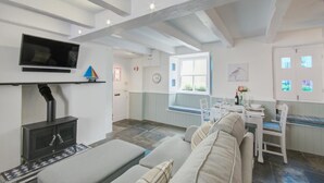 A modern living room with a sofa, a TV, a fireplace, and a dining area with a table and chairs. - 2 Bed in West Looe (oc-l30054) (Looe)