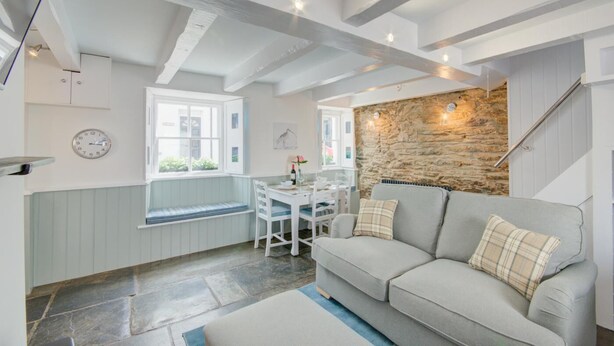 A cozy living room with a stone wall, a dining area with a table and chairs, and a built-in bench by the window. - 2 Bed in West Looe (oc-l30054) (Looe)