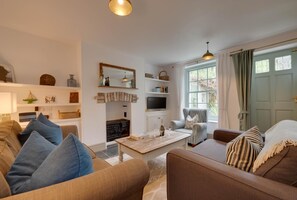 Sala de estar com sofá, poltrona, mesa de centro, televisão, lareira e janela com cortinas.
