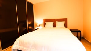 Una camera d'albergo con un letto grande, una testiera in legno, un comodino con una lampada e un armadio con ante scorrevoli.