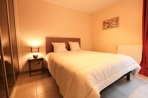 A bedroom with a bed, a bedside table with a lamp, and a wall-mounted picture. - Apartment near park, spa, casino. Free parking. (Vals-les-Bains)