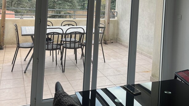 Un balcone con tavolo e sedie, una porta vetrata e vista su un paesaggio verde.