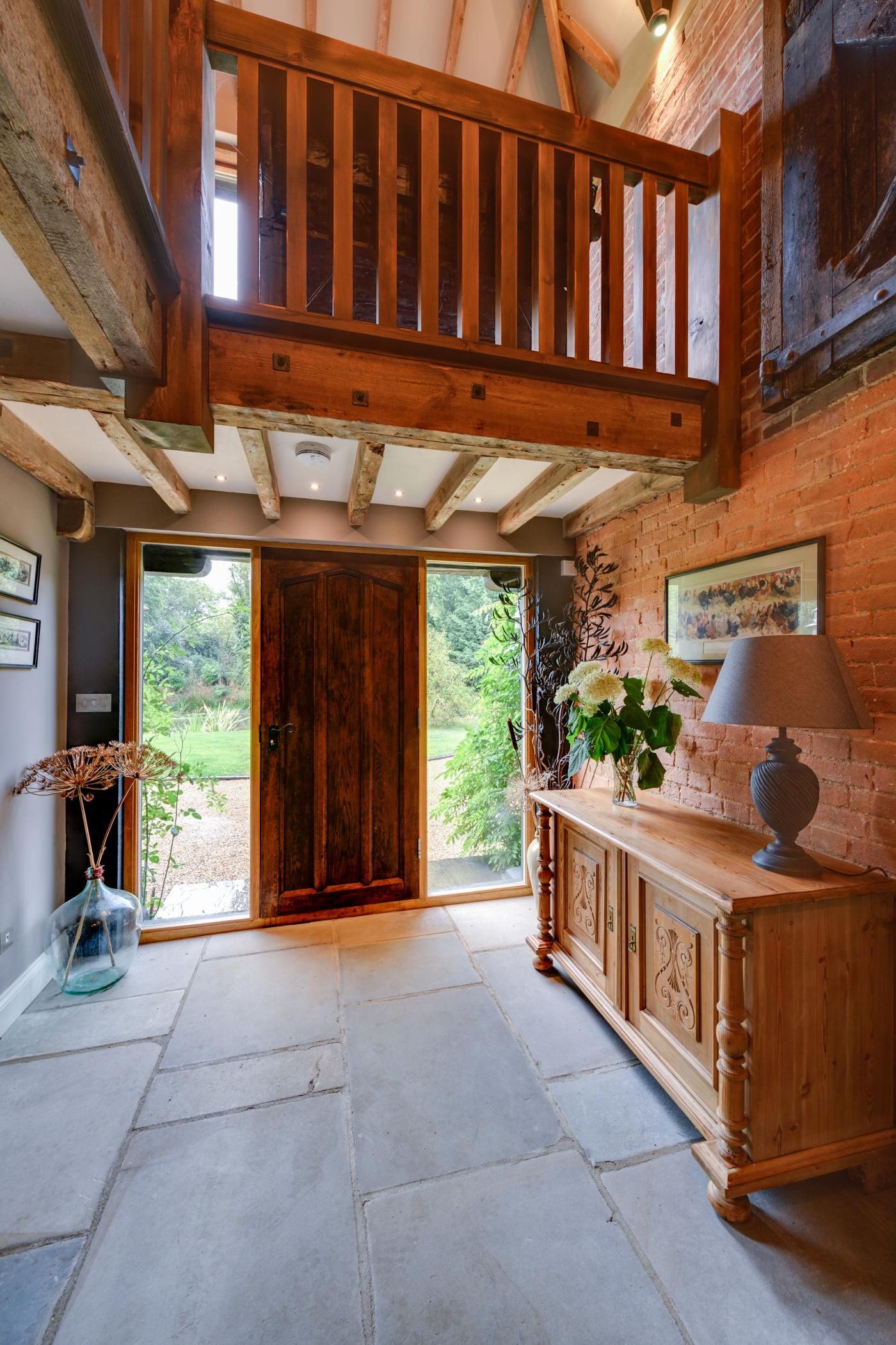 Un vestíbulo espacioso con una escalera de madera, una puerta principal de madera y vistas al exterior.