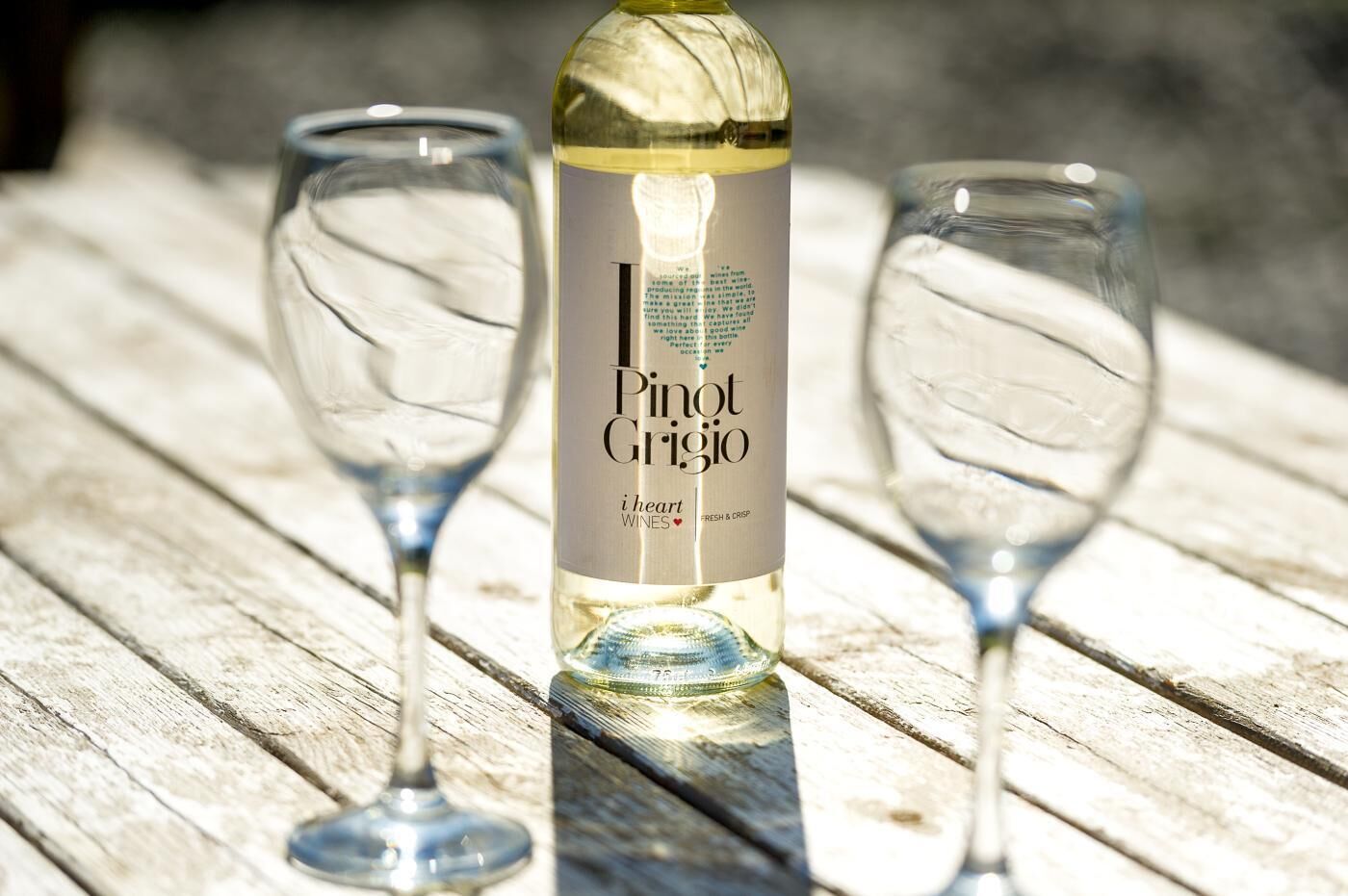 A bottle of Pinot Grigio wine on a wooden surface with two empty wine glasses beside it.