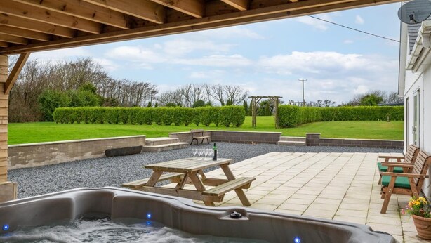 Un espace avec un jacuzzi, une terrasse en bois, une table de pique-nique et des sièges.