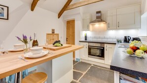 Une cuisine moderne avec des poutres en bois, des meubles blancs, un îlot central et un sol en pierre.
