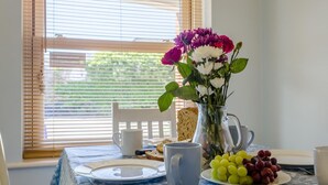 Un tavolo da pranzo con un vaso di fiori, un piatto di uva, una tazza bianca e una fetta di pane.
