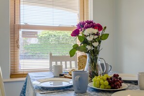 A dining table with a pitcher of flowers, a plate of grapes, a white mug, and a slice of bread. - 2 Bed in Aldeburgh (oc-7cc) (Aldeburgh)