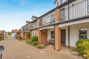 A two-story residential building with a brick facade, a balcony on the upper floor, and a paved driveway. - 2 Bed in Aldeburgh (oc-7cc) (Aldeburgh)