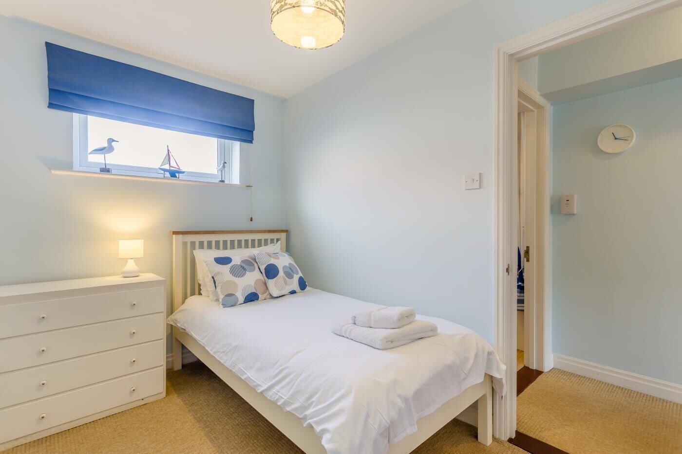 Um quarto com cama, mesa de cabeceira, cômoda, janela com vista e porta.