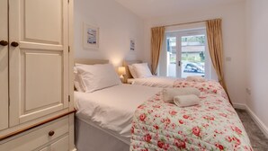Ein Hotelzimmer mit zwei Betten, einem Kleiderschrank, einem Fenster mit Vorhängen und Blick nach außen.
