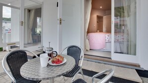 Ein Balkon mit einem Esstisch, gedeckt f ür das Frühstück, mit einer weißen Tasse, einem Teller mit Gebäck und Himbeeren sowie Korbstühlen.