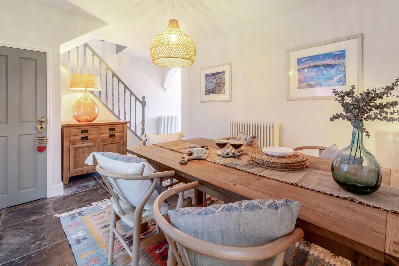 Un coin repas comprenant une table en bois, des chaises, un luminaire suspendu et un vase avec des fleurs.