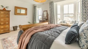 Un dormitorio con cama, cómoda, espejo y ventana con cortinas.