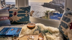 Un rincón acogedor con vistas al mar, una bebida en un vaso y un libro titulado 'Odyssey'.