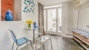Una habitación moderna con una mesa de vidrio, sillas, un florero con flores, un cuadro de peces en la pared, un radiador y vistas a través de una puerta de cristal.