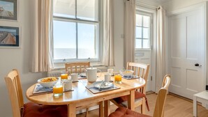 En matplats med ett träbord, stolar, frukostmat och stora fönster med gardiner.