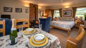 Een knus ingerichte kamer met een bed, een eettafel, een open haard en beelden in lijsten aan de wanden.