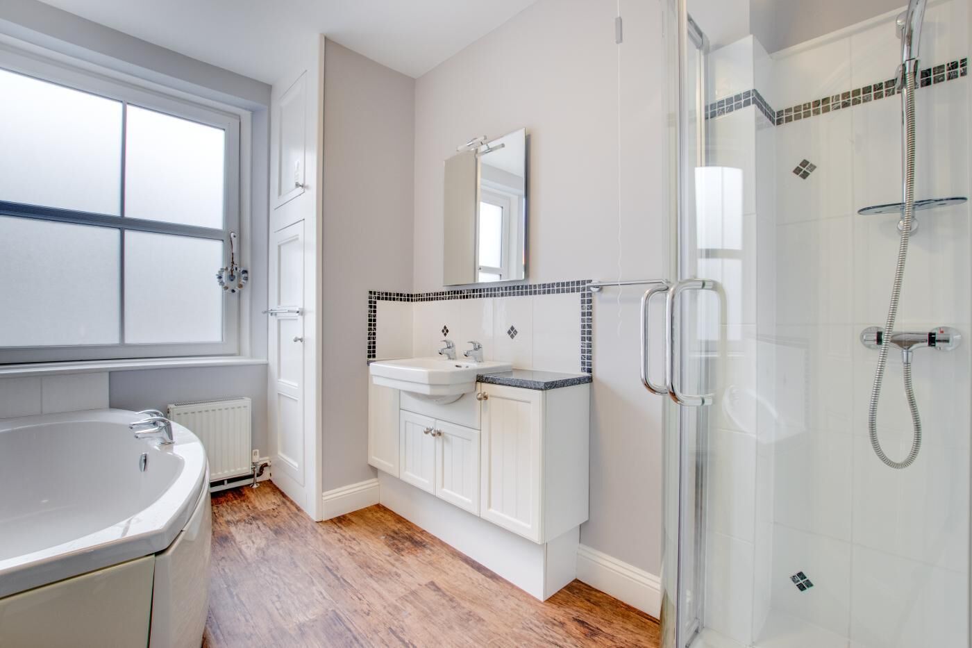A bathroom with a large window, a sink, a mirror, and a glass-enclosed shower.