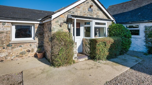 A stone cottage with a white door, a small porch, and a window.