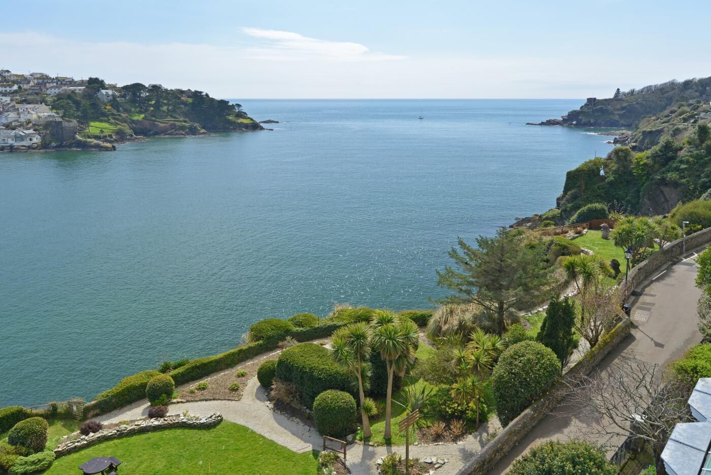 Paesaggio costiero con una passeggiata lastricata, vegetazione rigogliosa e vista sul mare.