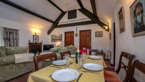 A dining area with a table set for four, wooden chairs, a sofa, a fireplace, and framed artwork on the walls. - 3 Bed in Llanbedrog (oc-thecll) (Llanbedrog)