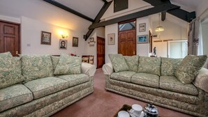 A living room with two patterned sofas, a coffee table with cups and a teapot, and a high ceiling with exposed beams. - 3 Bed in Llanbedrog (oc-thecll) (Llanbedrog)