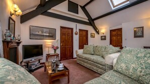 A cozy living room with a high ceiling, wooden beams, a television, a sofa, and a coffee table. - 3 Bed in Llanbedrog (oc-thecll) (Llanbedrog)