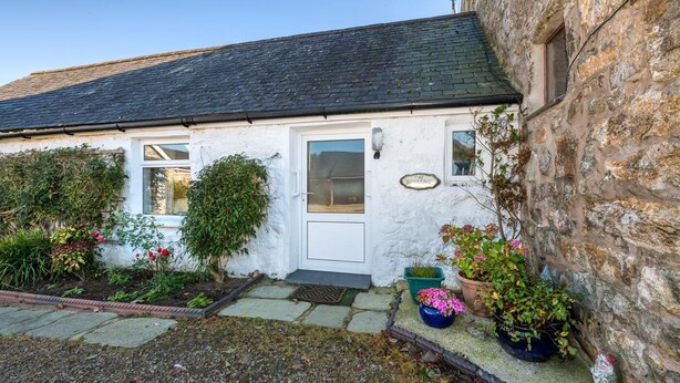 A white cottage with a stone wall, a door, and a small garden with potted plants. - 3 Bed in Llanbedrog (oc-thecll) (Llanbedrog)