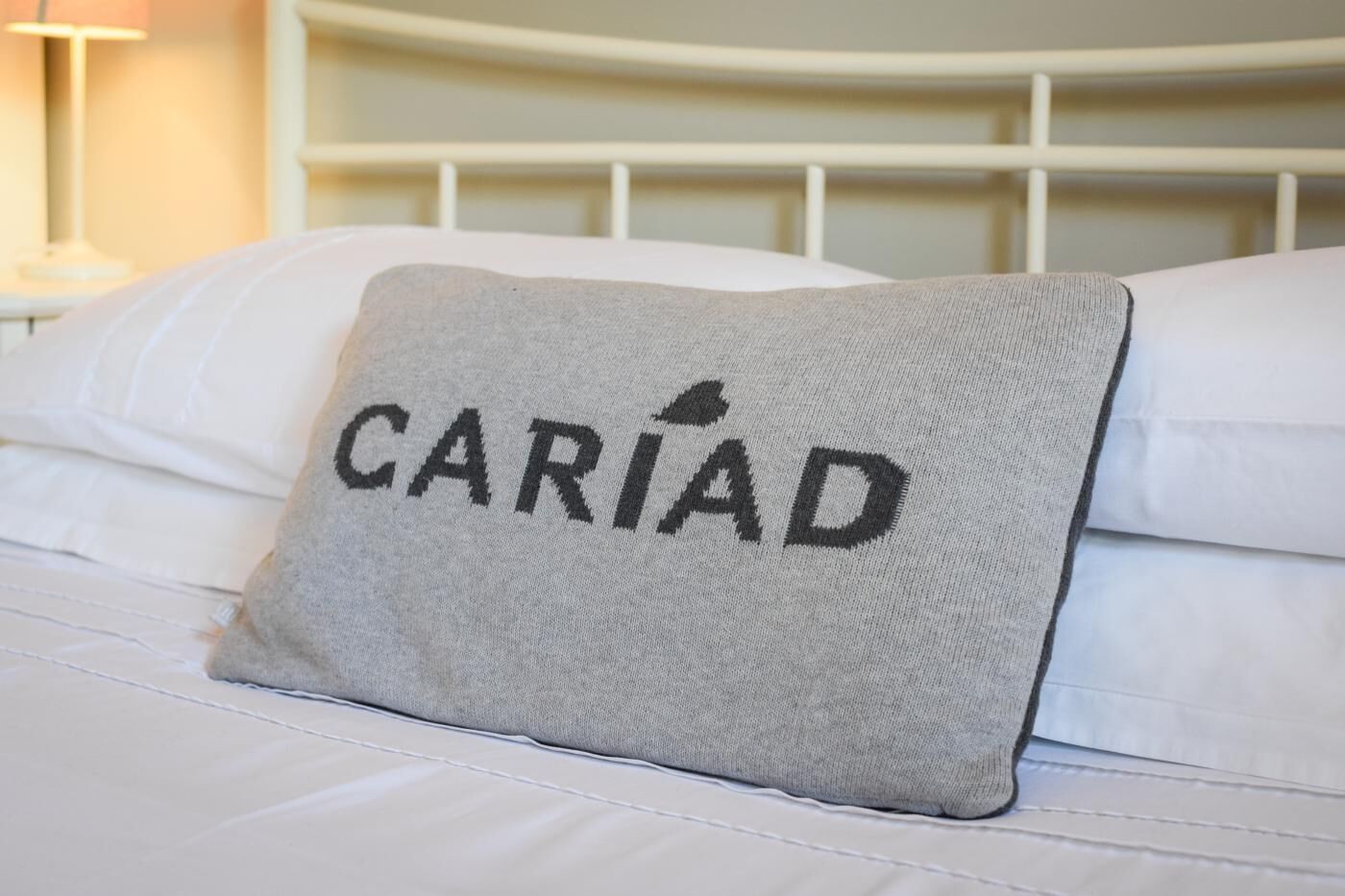 A bed with a pillow featuring the word "CARIAD" embroidered on it.