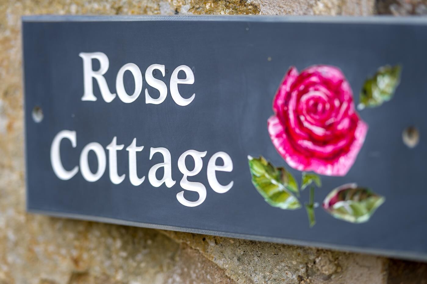 Une enseigne indiquant « Rose Cottage », avec une rose et des feuilles peintes.