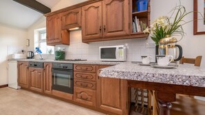 A kitchen with wooden cabinets, a microwave, a coffee maker, and a vase with flowers. - 3 Bed in Llanbedrog (oc-rosell) (Llanbedrog)