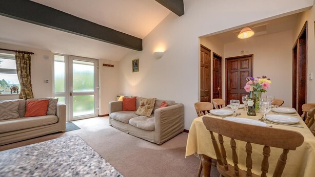 A dining area with a table set for four, a sofa, and a window with curtains. - 3 Bed in Llanbedrog (oc-rosell) (Llanbedrog)