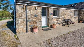 A stone cottage with a front door, a window, a bench, and two potted plants. - 3 Bed in Llanbedrog (oc-rosell) (Llanbedrog)