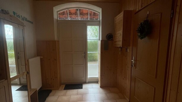 A wooden interior with a tiled floor, a double door with glass panels, and a welcome sign. - Vacation in the countryside with a pet (Rathenow)