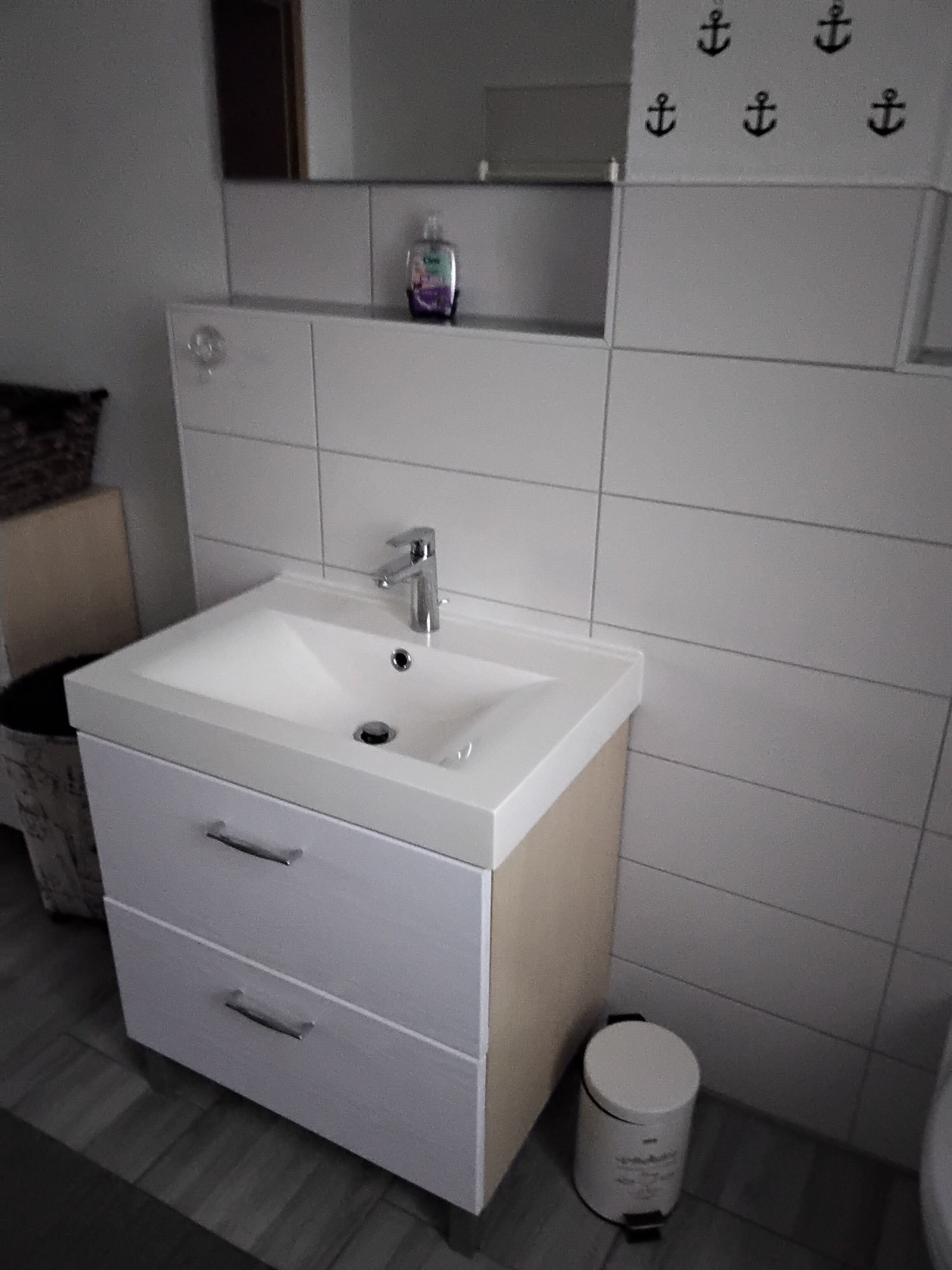 Un baño con un lavabo blanco, dos cajones, un espejo sobre el lavabo y un pequeño estante con artículos de aseo.