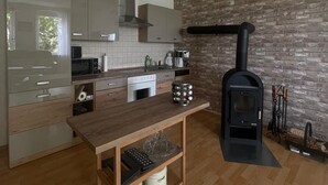 A modern kitchen with a wood-burning stove, a wooden table, and a stone wall backsplash. - Vacation in the countryside with a pet (Rathenow)