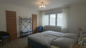 A bedroom with a bed, a chair, a radiator, and a window with curtains. - Vacation in the countryside with a pet (Rathenow)