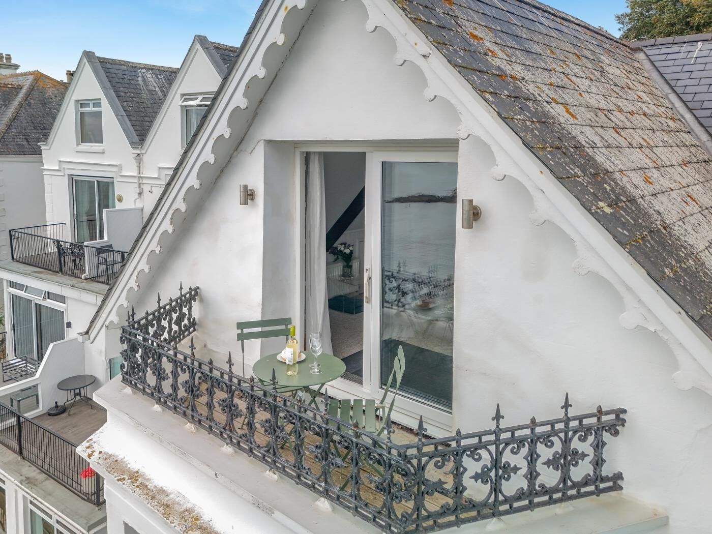 Un bâtiment blanc doté d’un balcon orné d’une balustrade en fer forgé et d’une petite table sur laquelle se trouvent une bouteille et un verre.