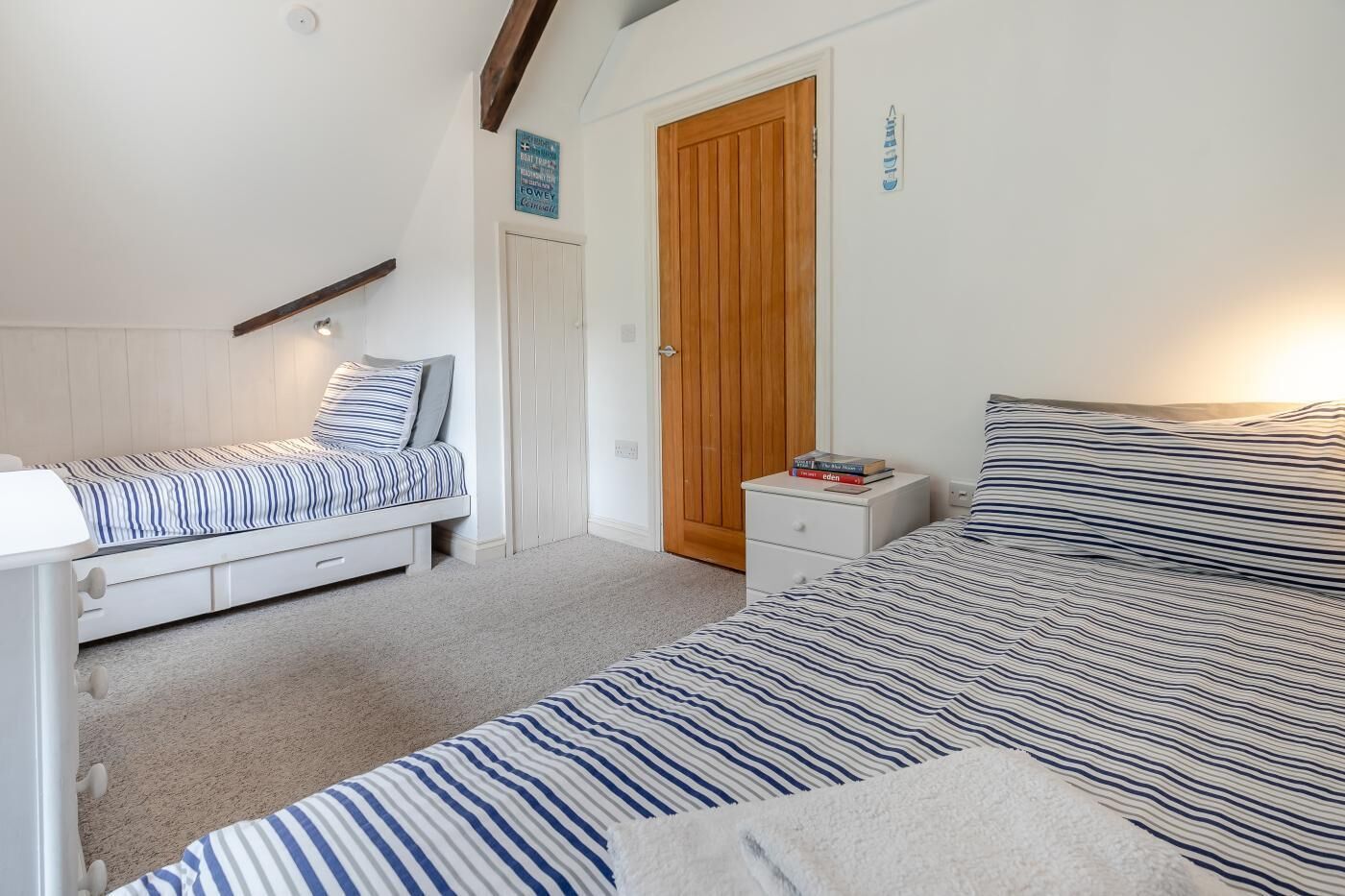 Een slaapkamer met twee bedden, een houten deur en een klein nachtkastje met boeken.